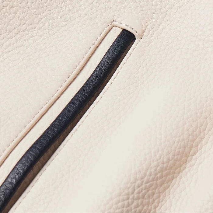 Close-up of front pocket detail with black trim on beige varsity jacket.