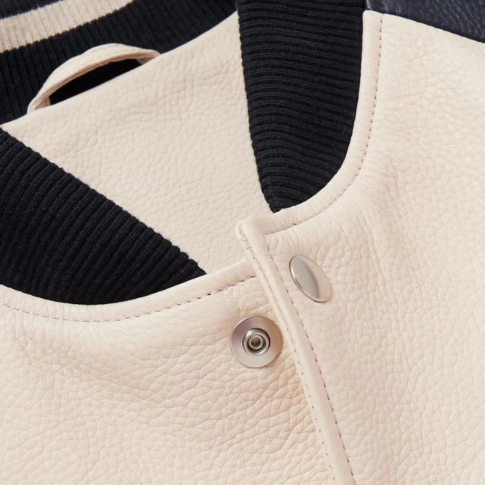 Close-up of the collar and snap button detail on beige varsity jacket.