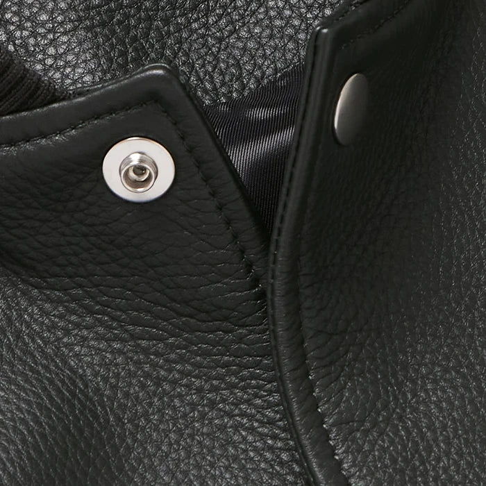 Close-up of black leather varsity jacket snap button and textured grain finish.