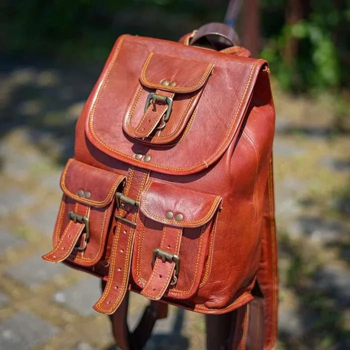 Brown leather backpack with multiple pockets and straps on a blurred natural background
