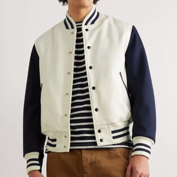 Person wearing a white and navy varsity jacket over a striped shirt on a plain background