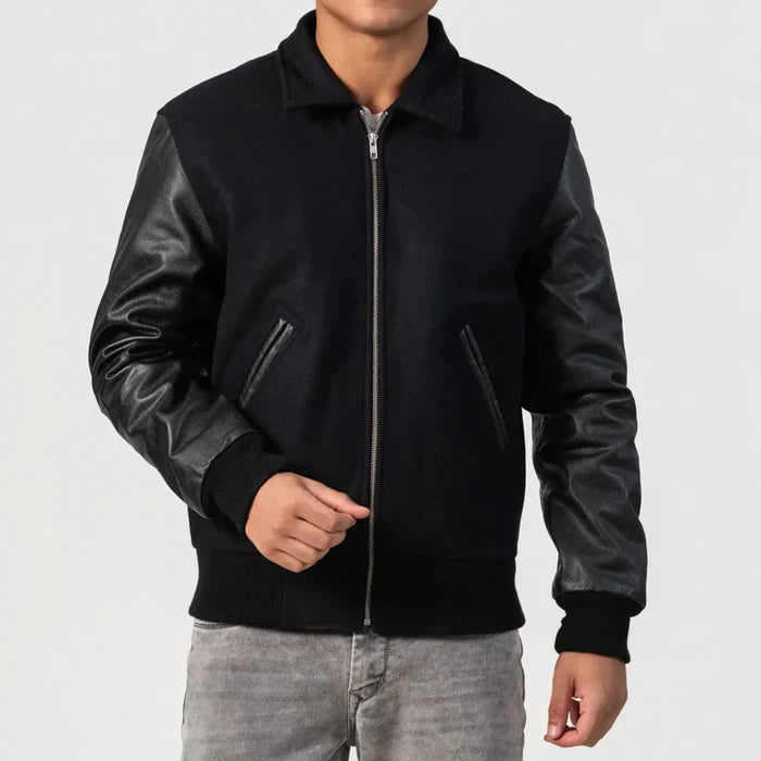 A man wearing a black wool varsity jacket with leather sleeves and a zipper front.