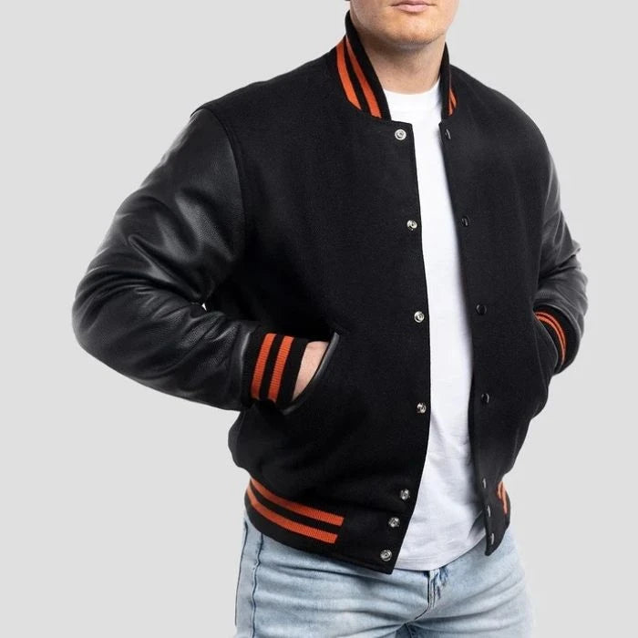Black varsity jacket with leather sleeves and orange accents worn by a person on a light gray background